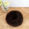 Round handmade dog cushion with natural sheepskin filling, dark brown, on wooden floor.