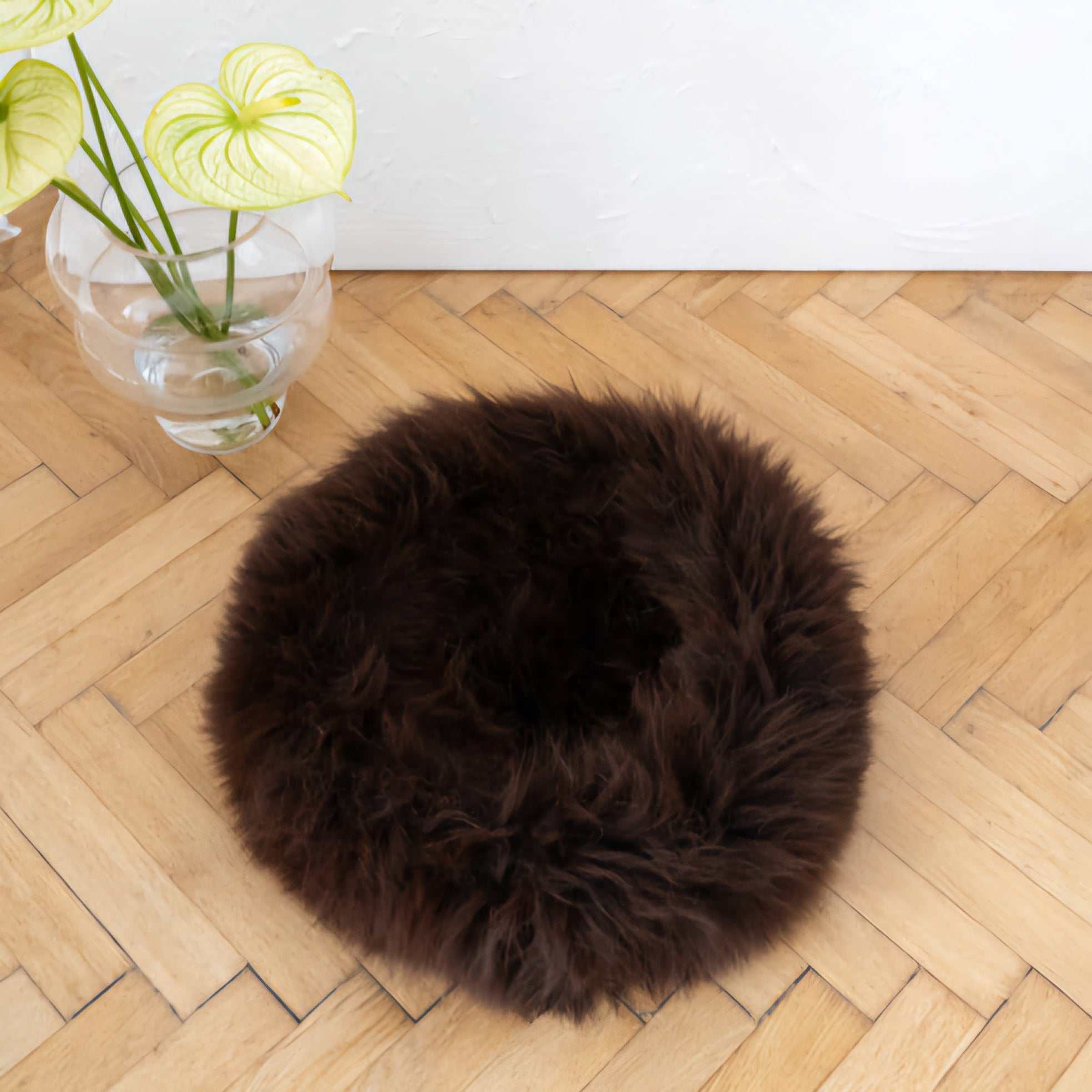 Round handmade dog cushion with natural sheepskin filling, dark brown, on wooden floor.